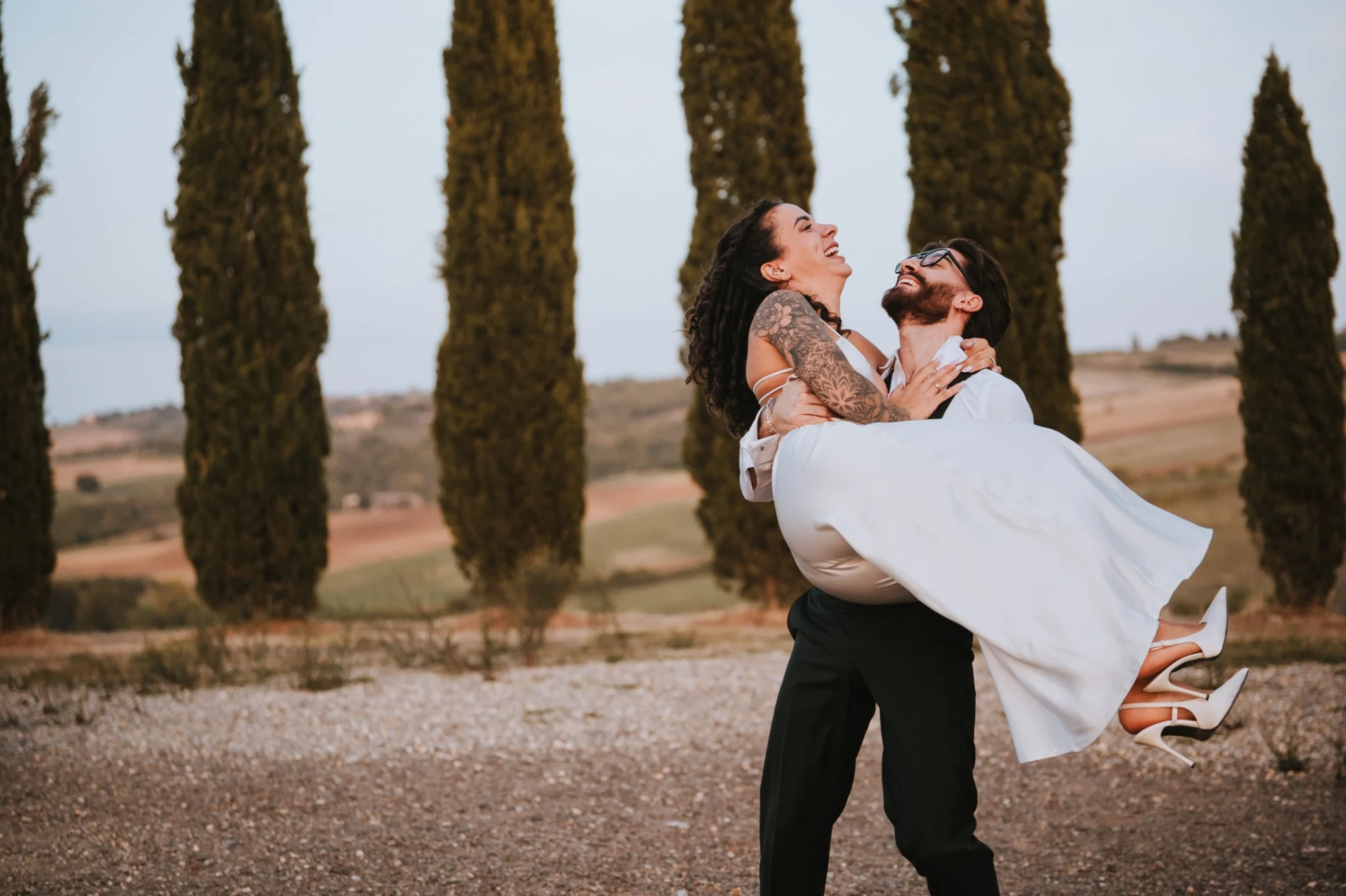 Lo sposo solleva la sposa tra i cipressi