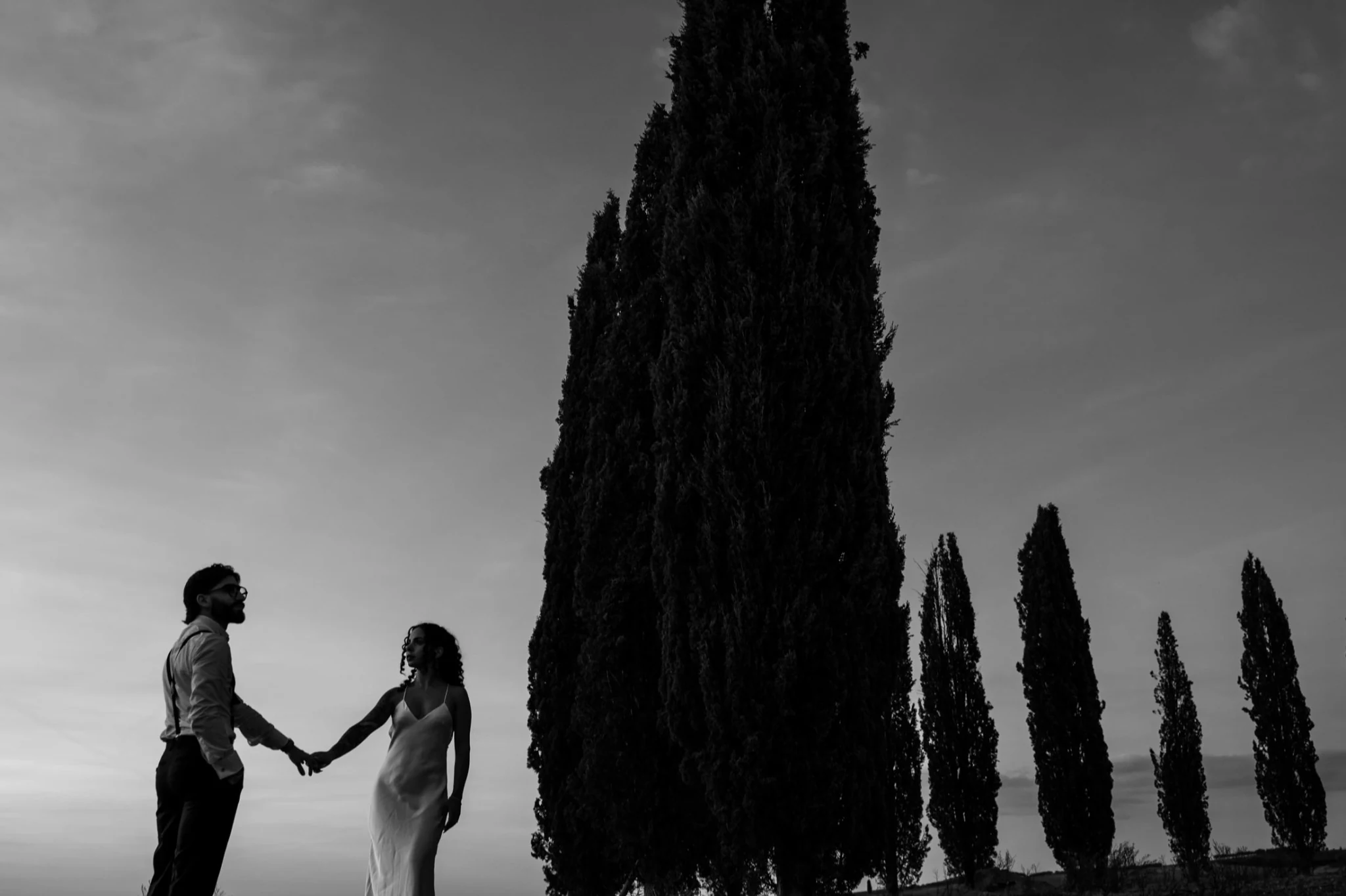 Gli sposi mano nella mano tra i cipressi, in bianco e nero